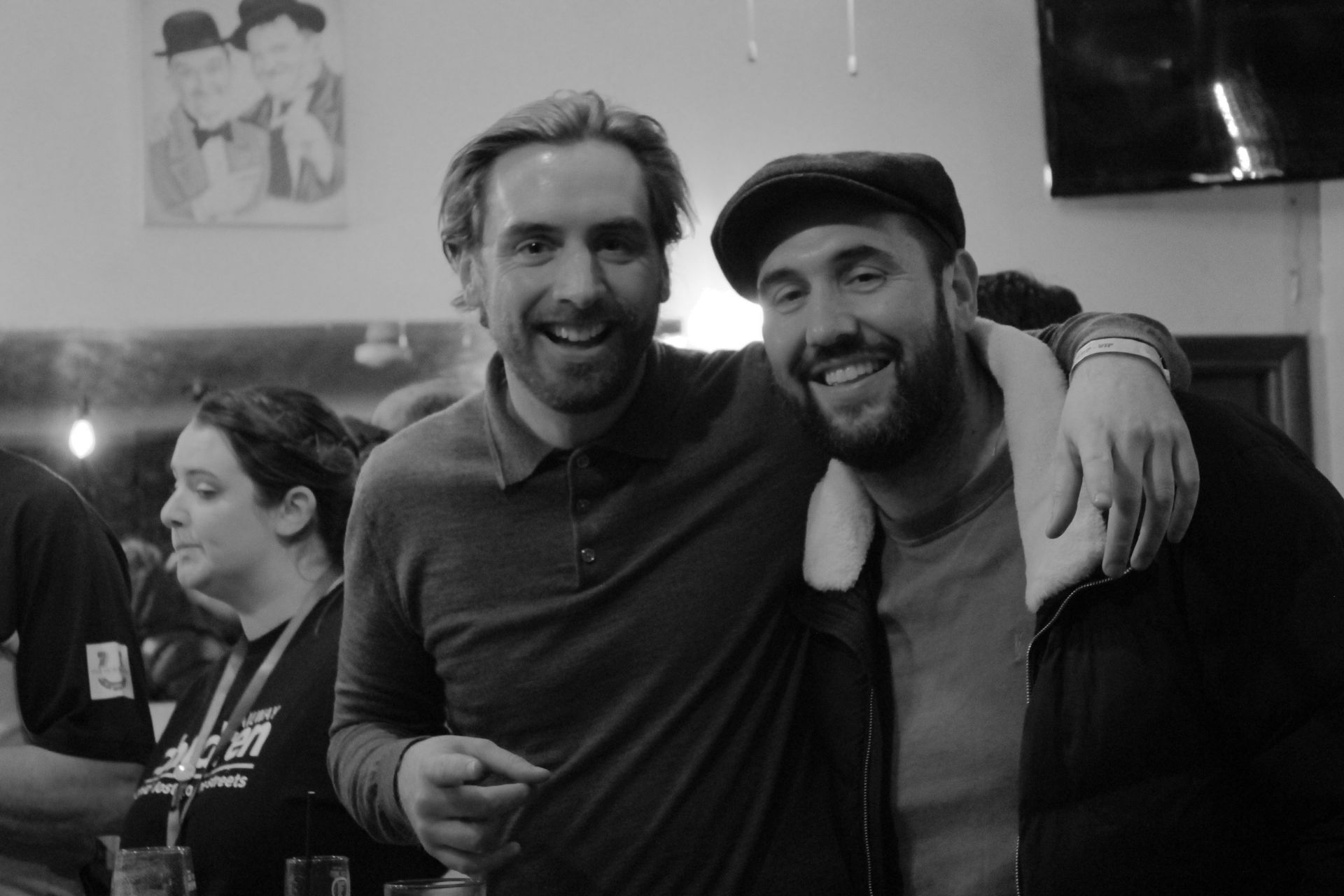 Two smiling men pose close together, one with arm around the other's shoulders. Black and white photo.