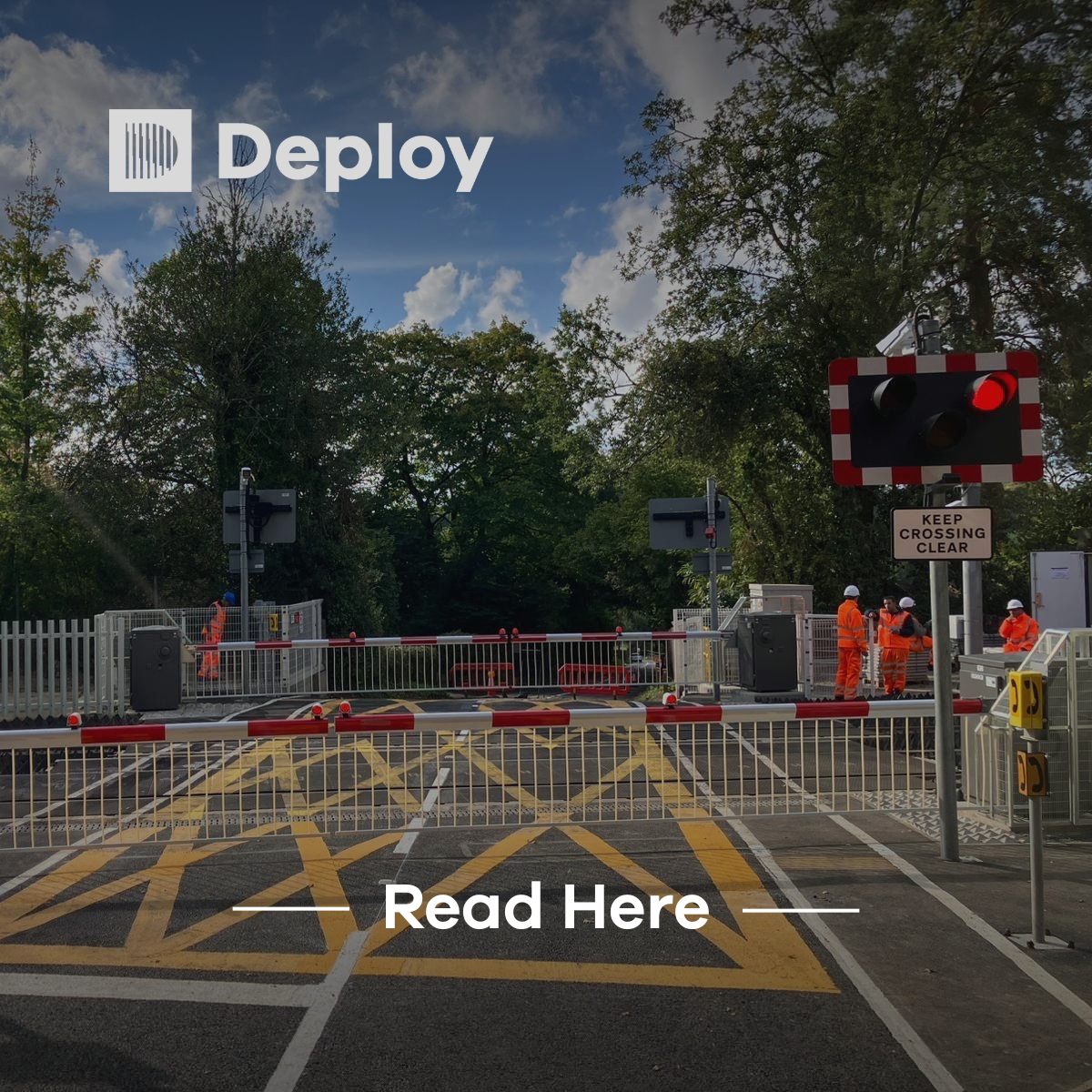 Railway crossing with closed barriers, red lights on, workers in orange vests, road markings, and a