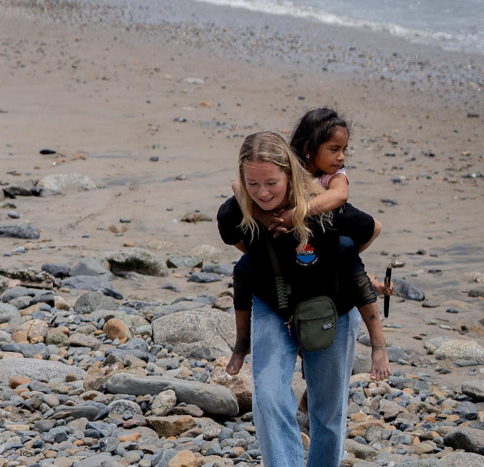 Picture of a volunteer giving a piggy-back to a local child across a beach.