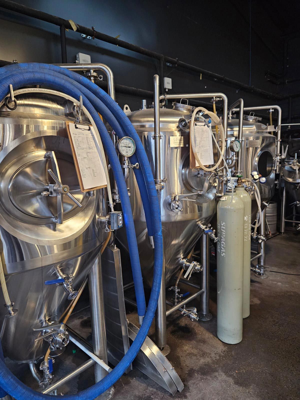 Stainless steel brewery tanks with blue hoses and a grey CO2 tank.