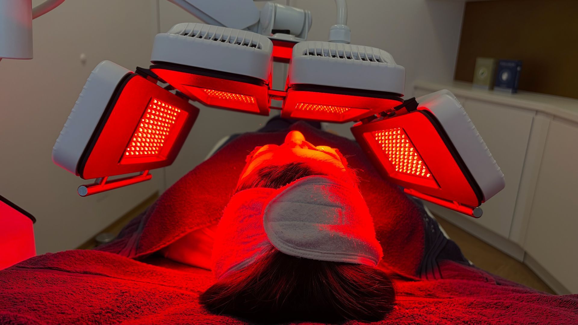 Frau erhält Rotlichttherapie, liegt mit geschlossenen Augen in einer schwach beleuchteten Umgebung.
