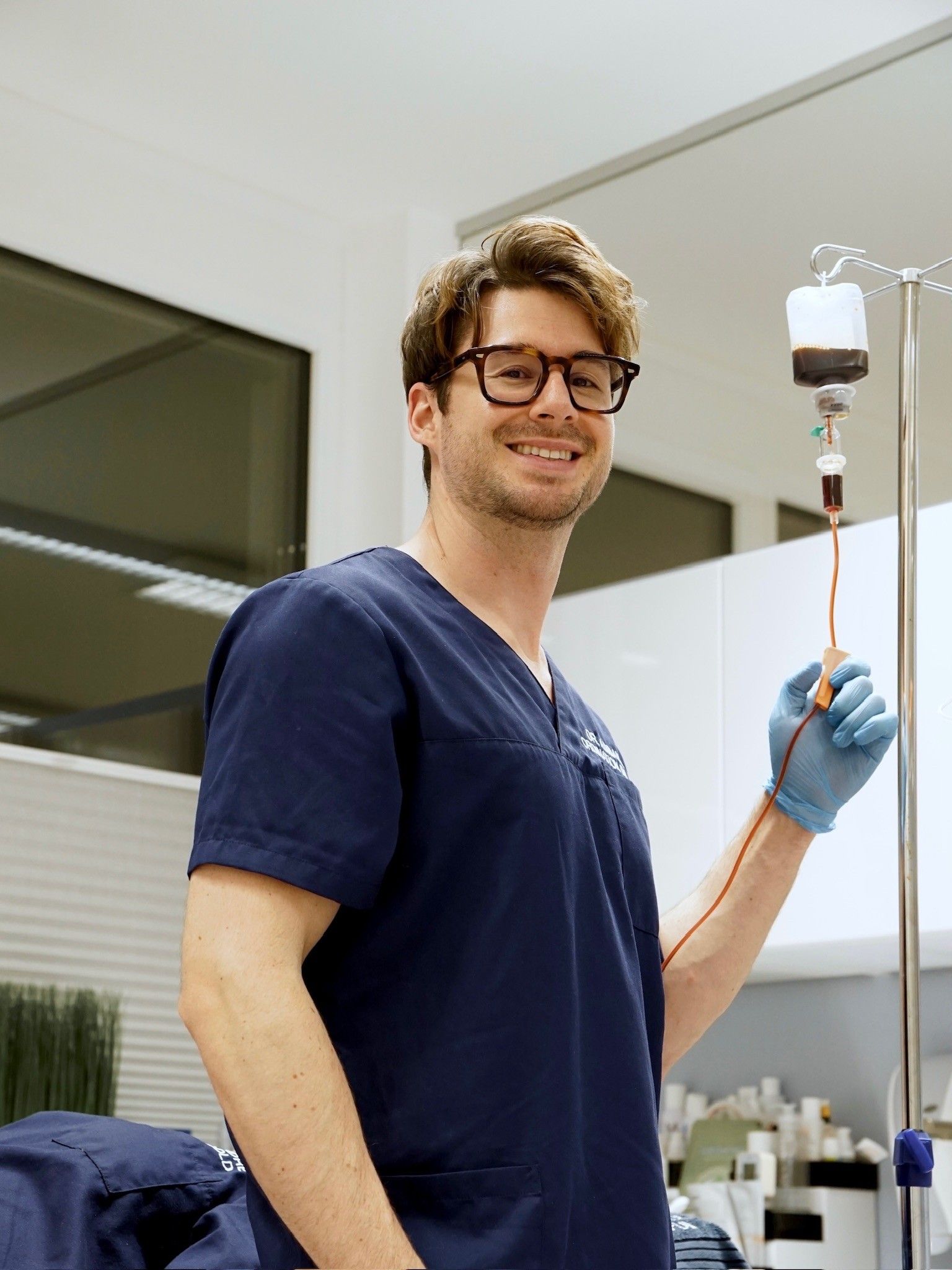 Ärztin im blauen Kittel stellt die Infusion für den Patienten ein. Sie lächelt und betrachtet den Patienten in einer medizinischen Umgebung.