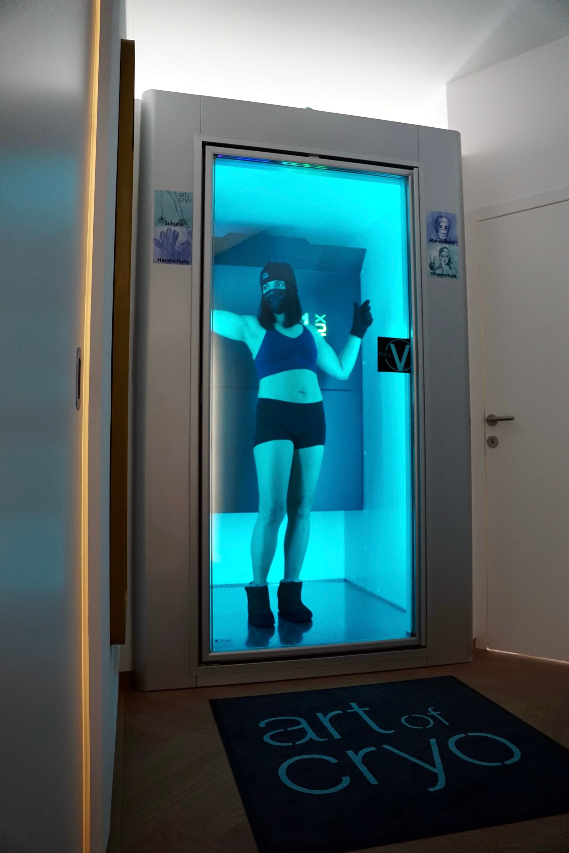 Blau beleuchtete Kryotherapiekammer mit „Art of Cryo“-Matte. 