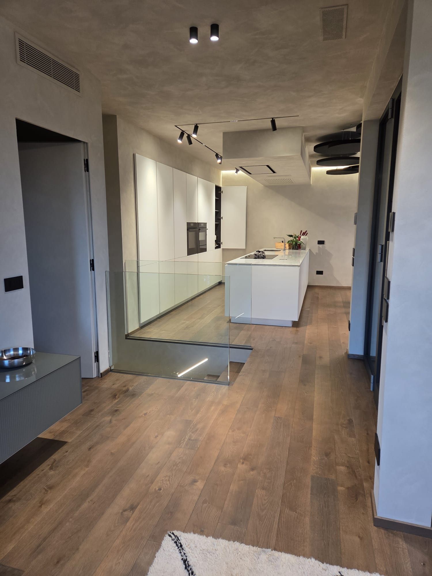 Interno moderno e vuoto con pavimento in legno, pareti bianche e una piccola isola cucina al centro.