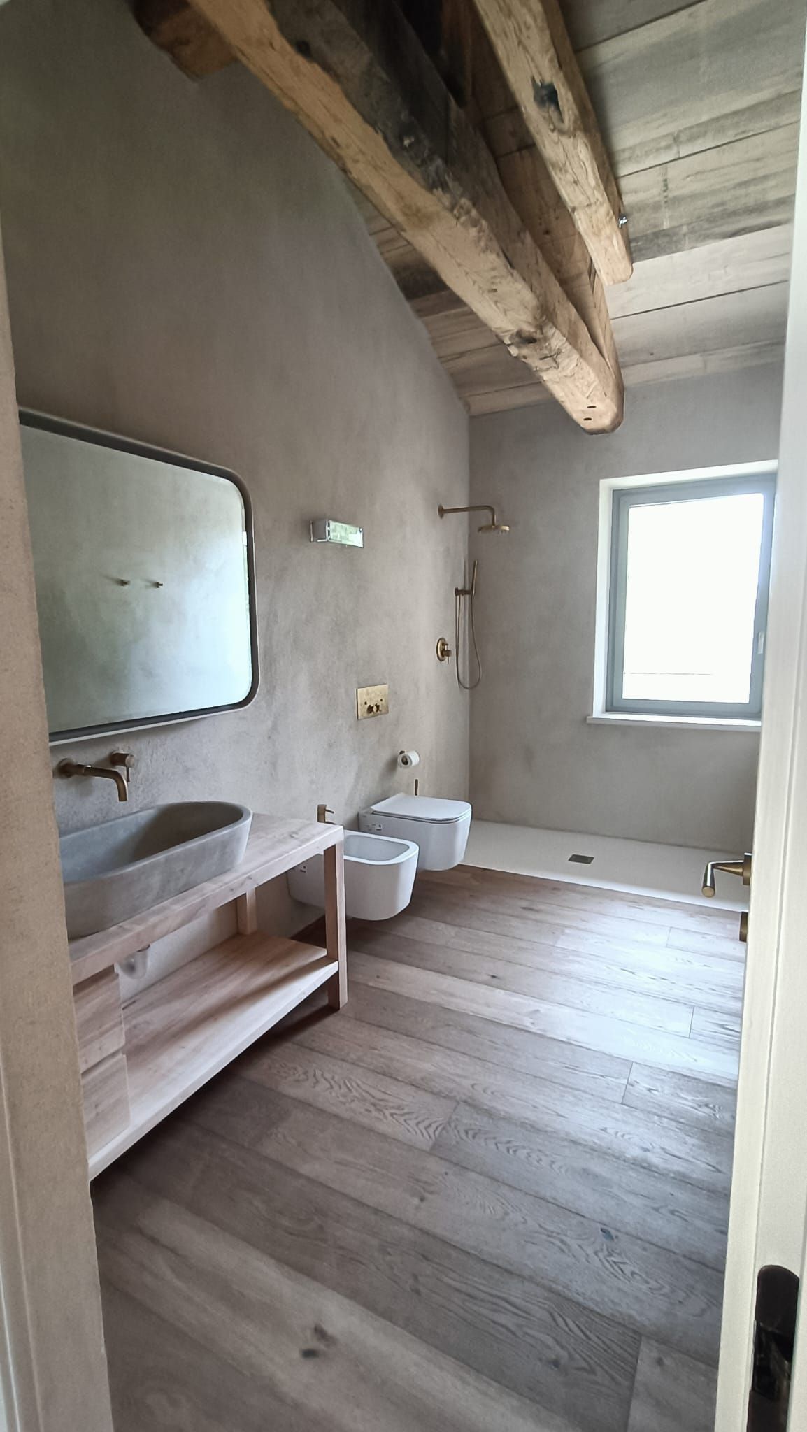 Piccolo bagno rustico con travi in ​​legno, specchio, lavandino, WC e finestra.
