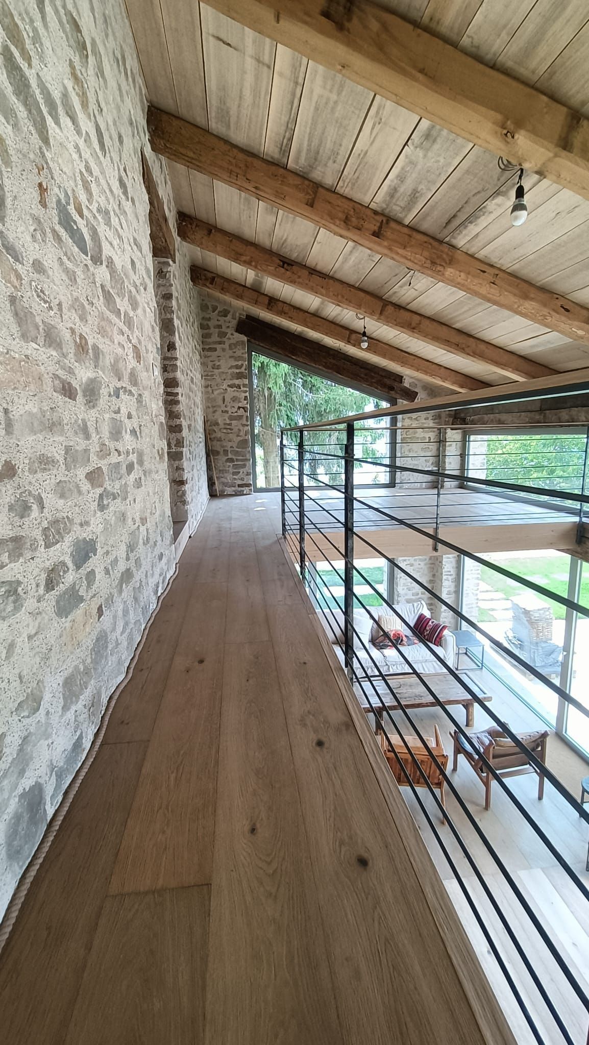 Passerella in pietra con travi in ​​legno e ringhiera in metallo che si affaccia sul verde.