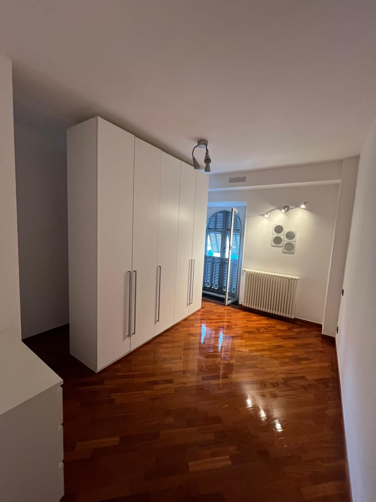 Corridoio moderno con armadietti bianchi, pavimento in legno lucido e zona salotto illuminata in fondo.