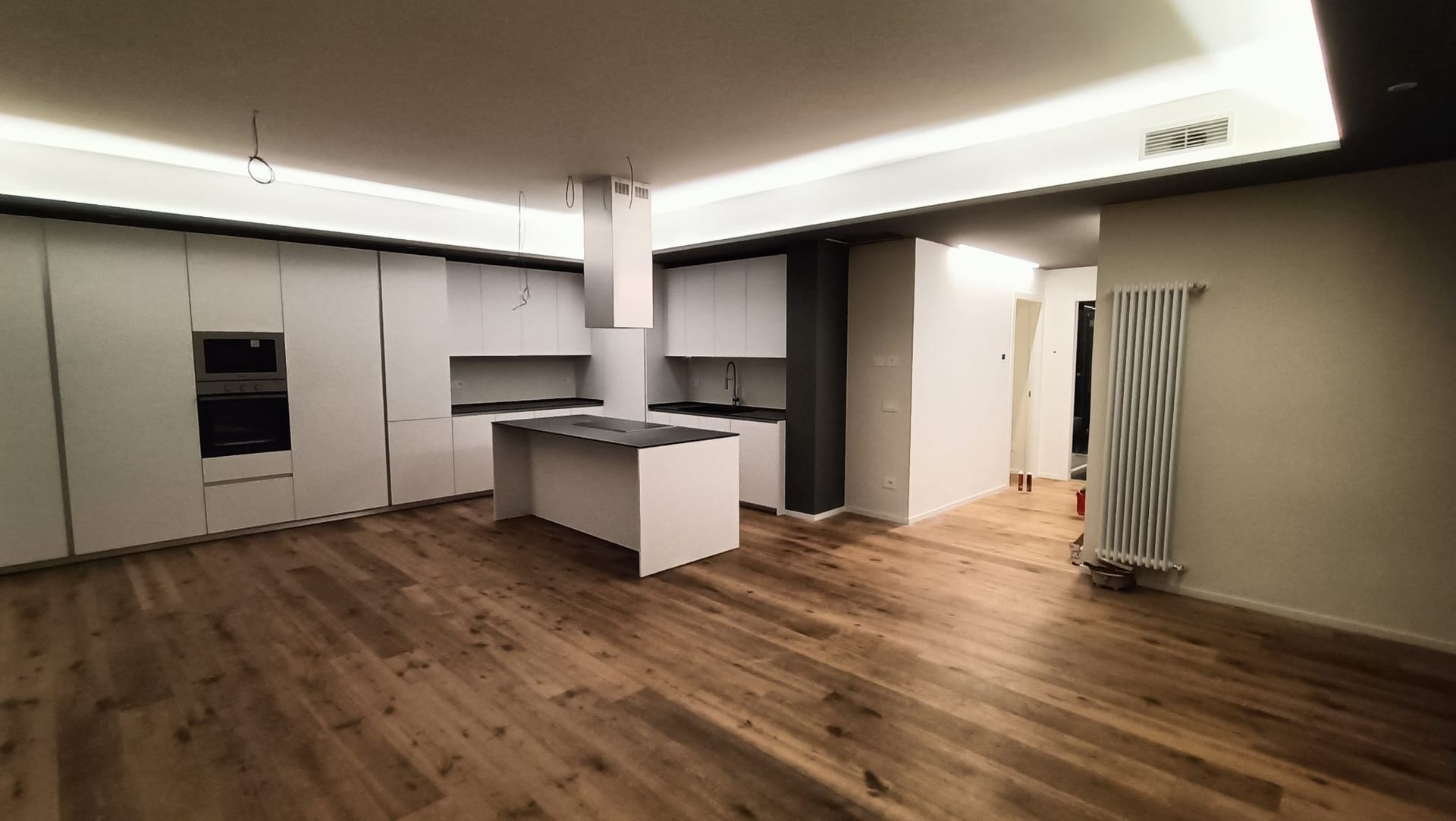 Stanza moderna vuota con pavimento in legno, mobili bianchi, isola cucina e tenda a righe vicino alla porta.