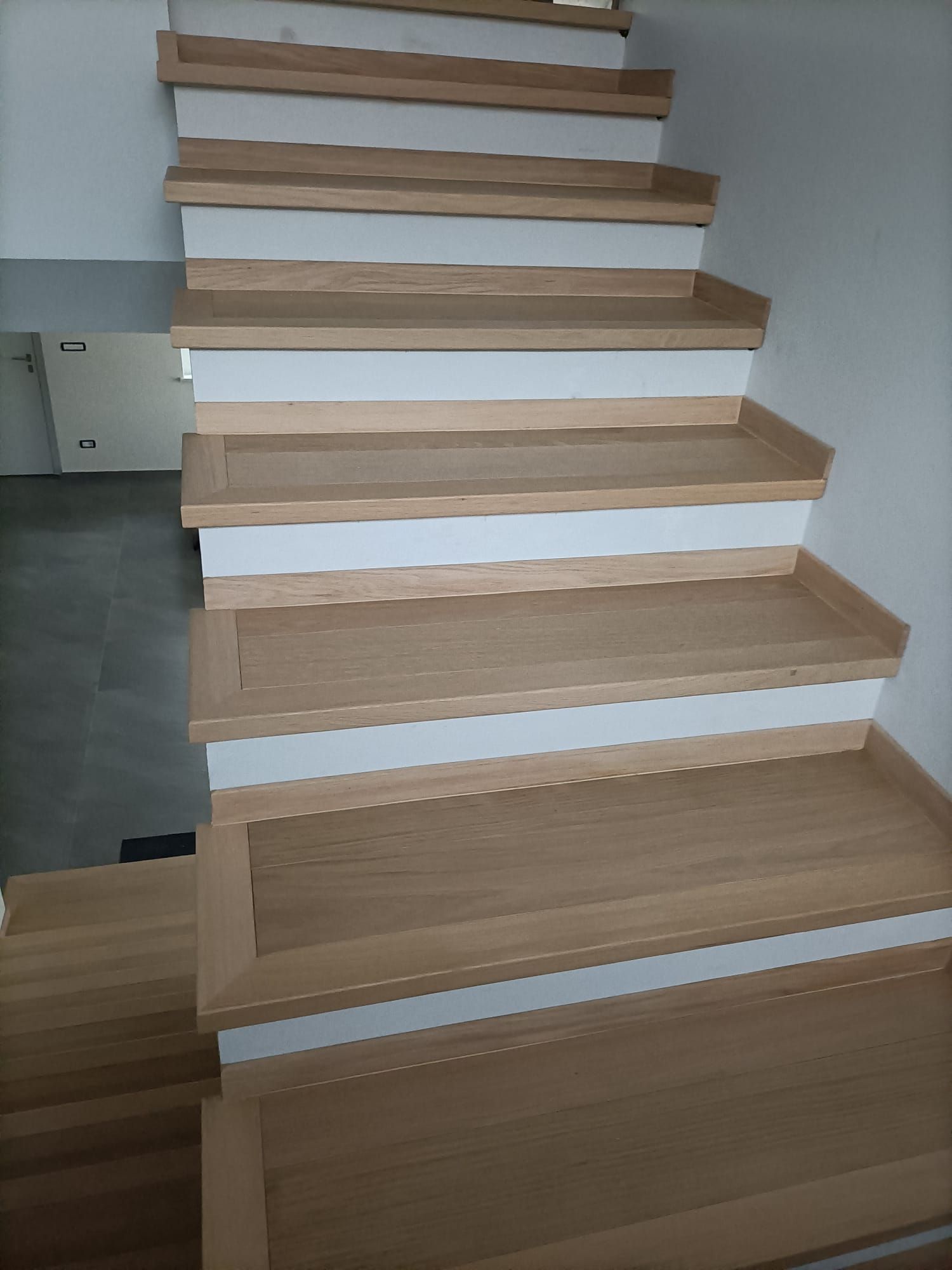 Scala interna con gradini in legno chiaro e alzate bianche, vista dal basso.