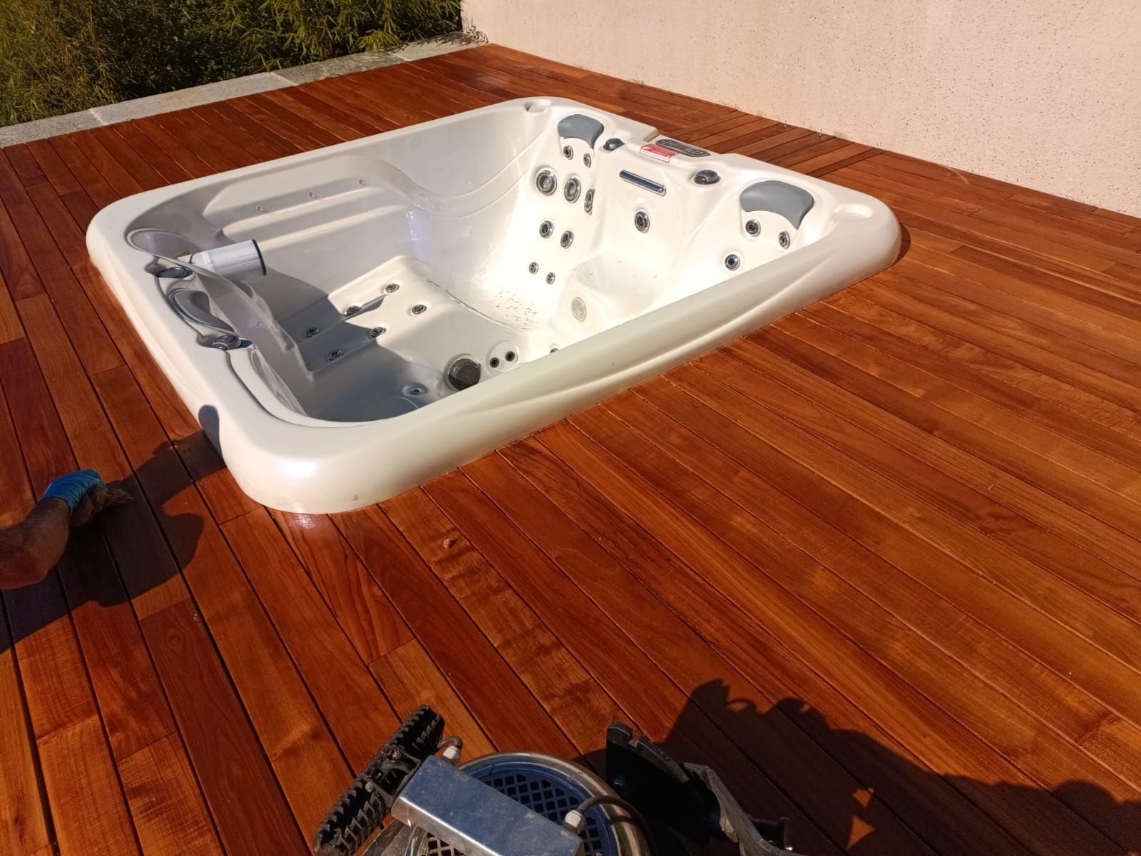 Vasca idromassaggio bianca su una terrazza in legno accanto a un muro, con uno skimmer blu in primo piano.
