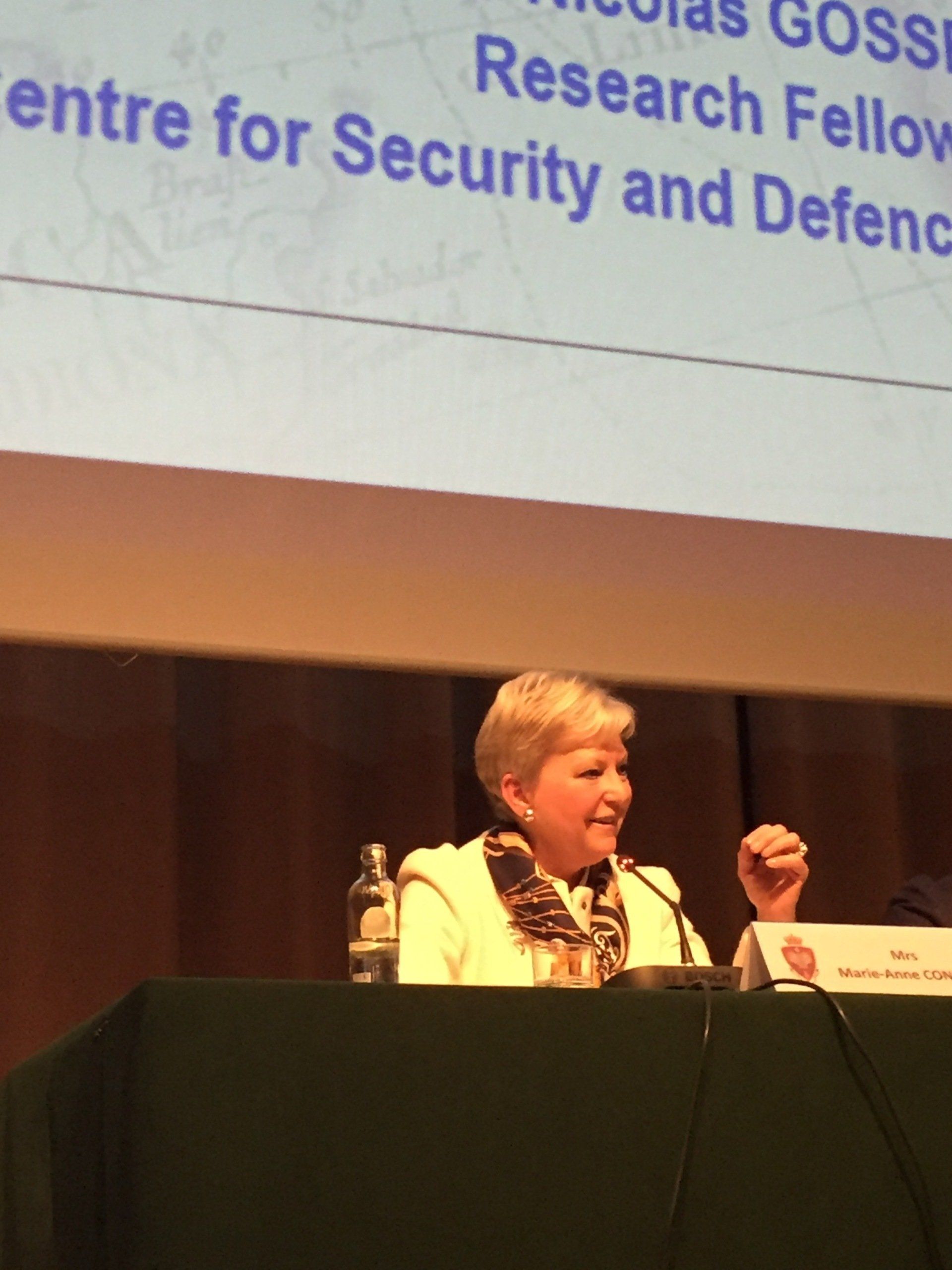 Eine Frau sitzt an einem Tisch vor einem Bildschirm mit der Aufschrift „Zentrum für Sicherheit und Verteidigung“