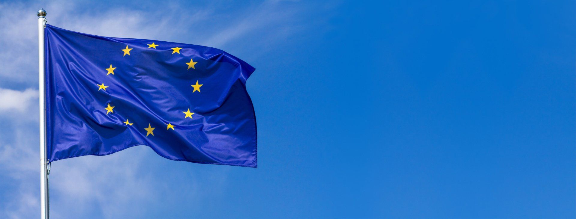 Eine blaue Flagge mit gelben Sternen weht im Wind vor einem blauen Himmel.