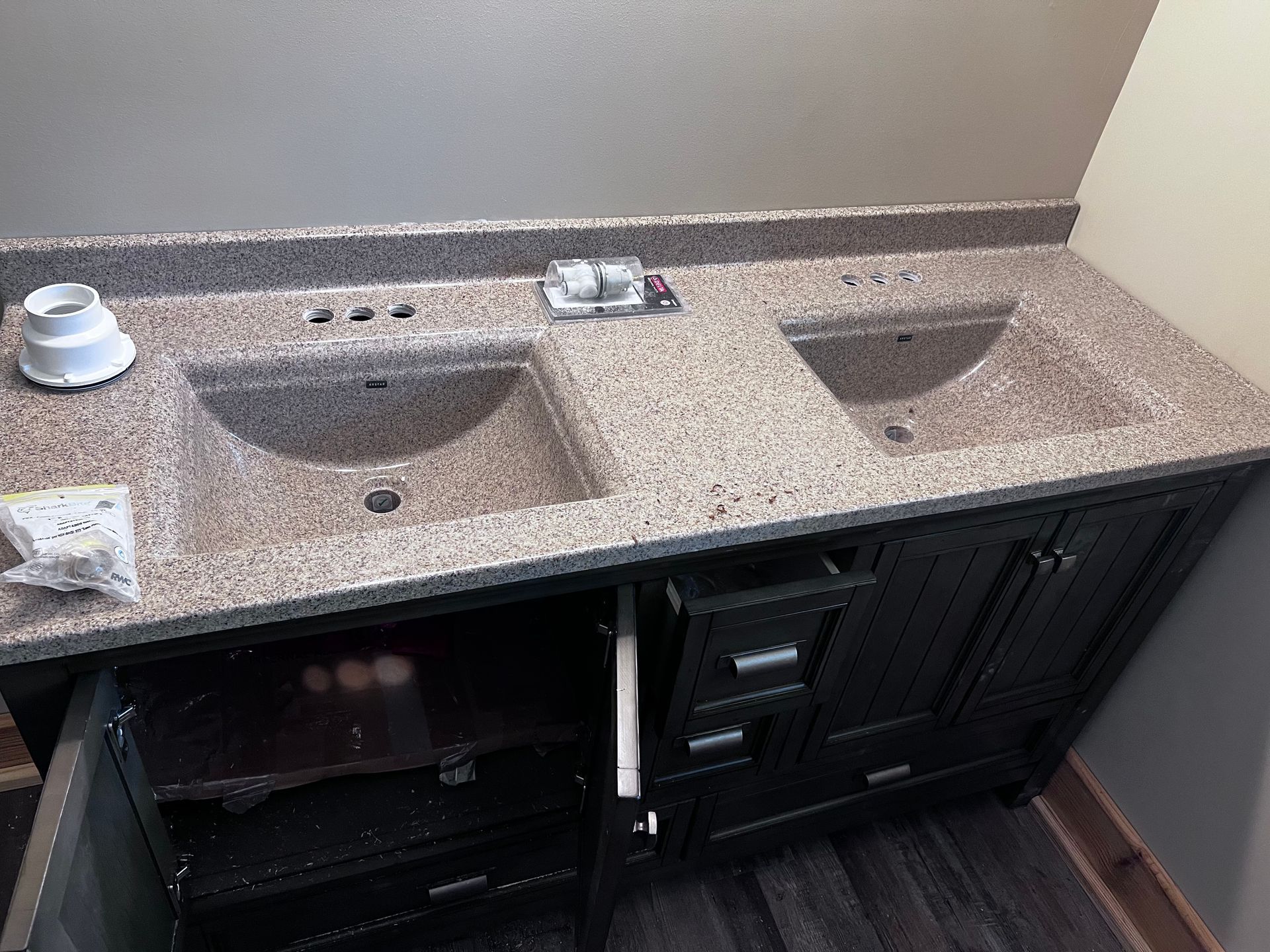 Double sink bathroom vanity with dark cabinets and speckled countertop.