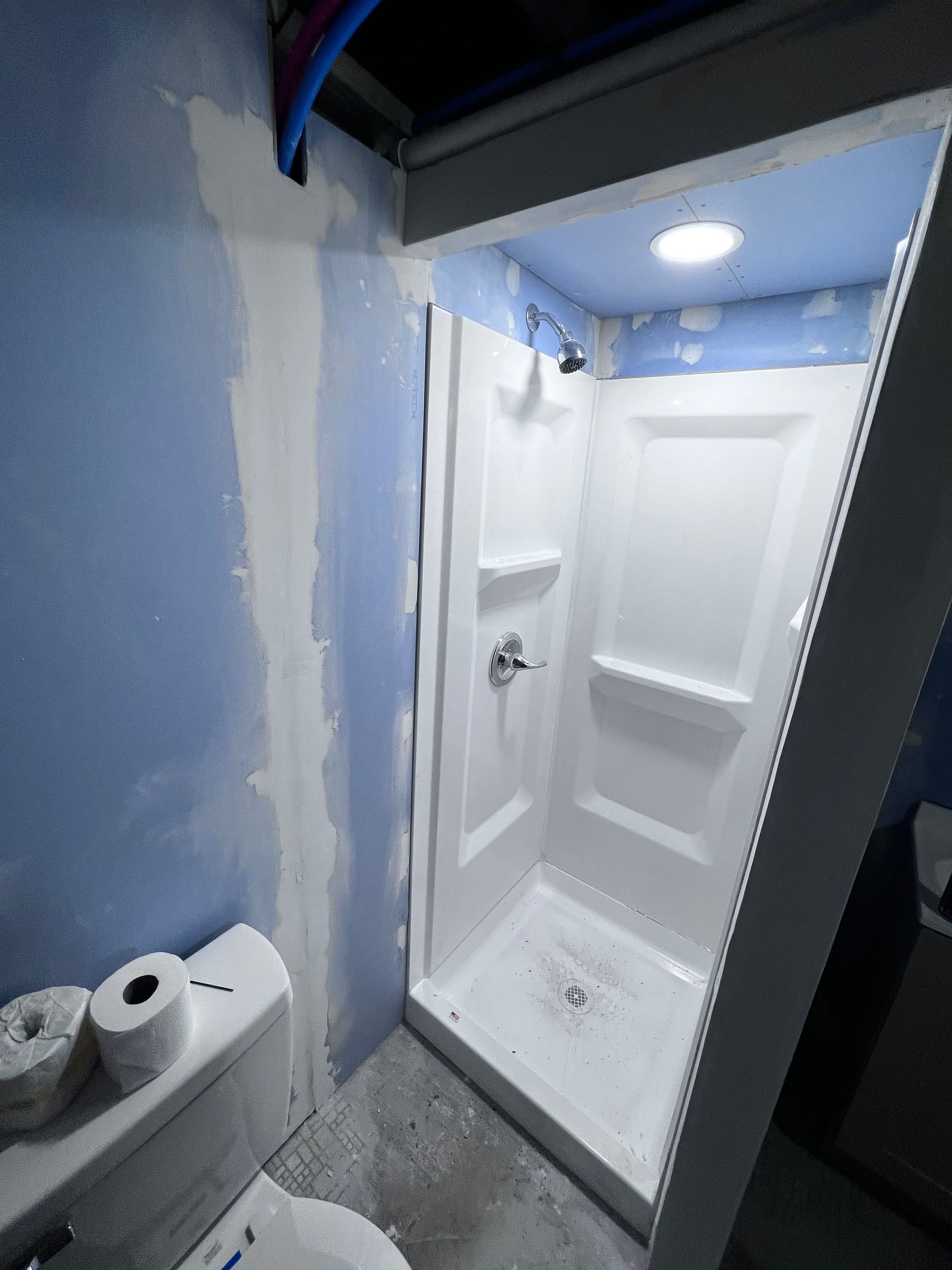 Small bathroom under construction, new white shower stall installed. Blue walls, toilet, and ceiling with cloud pattern.