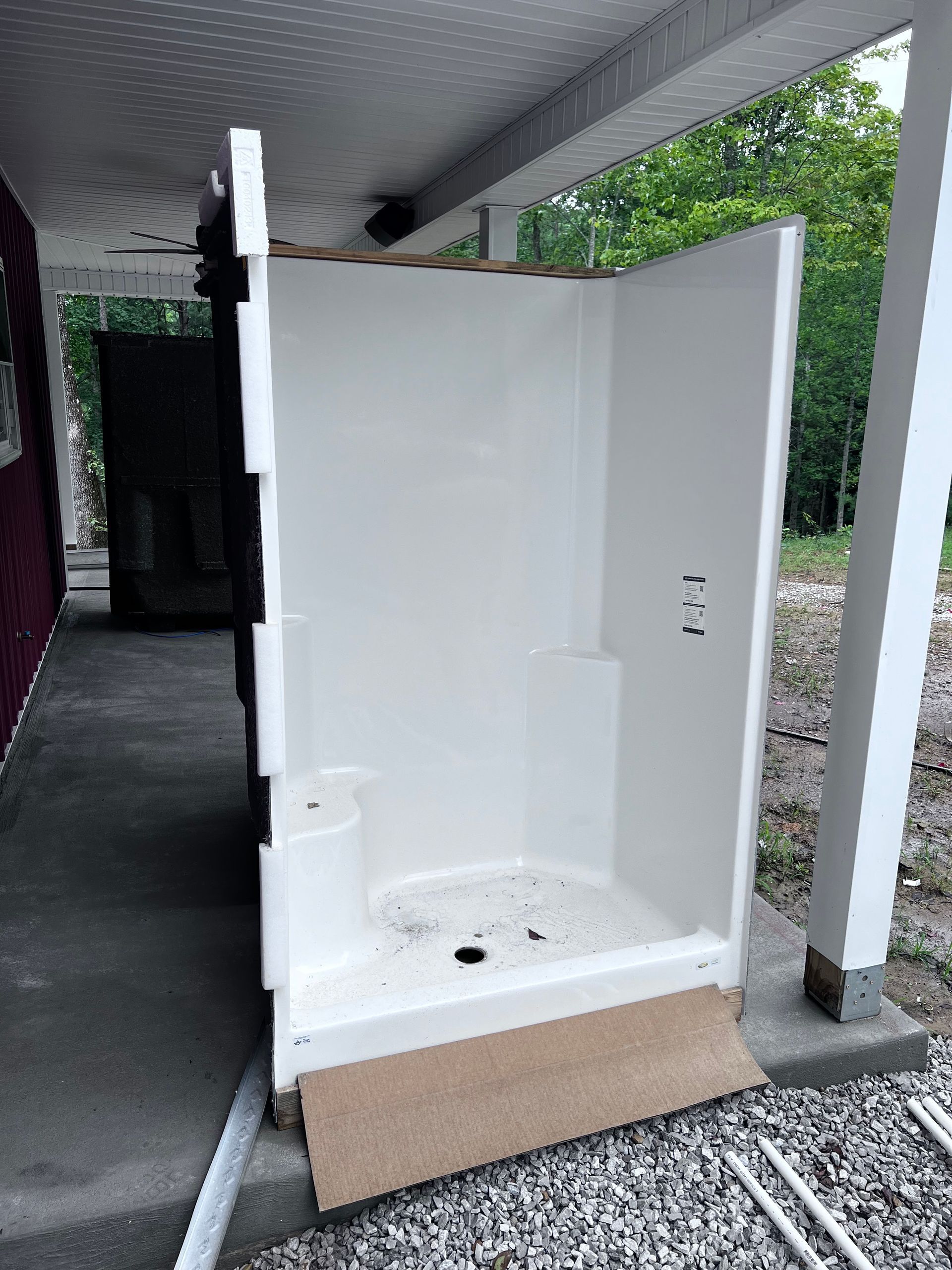 White, prefabricated shower unit under a covered porch, ready for installation.
