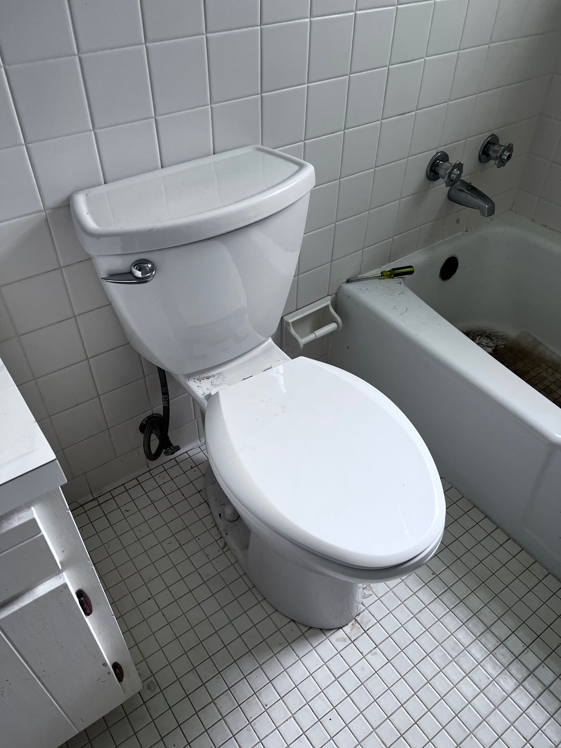 White toilet in a bathroom with a white tiled wall and bathtub.