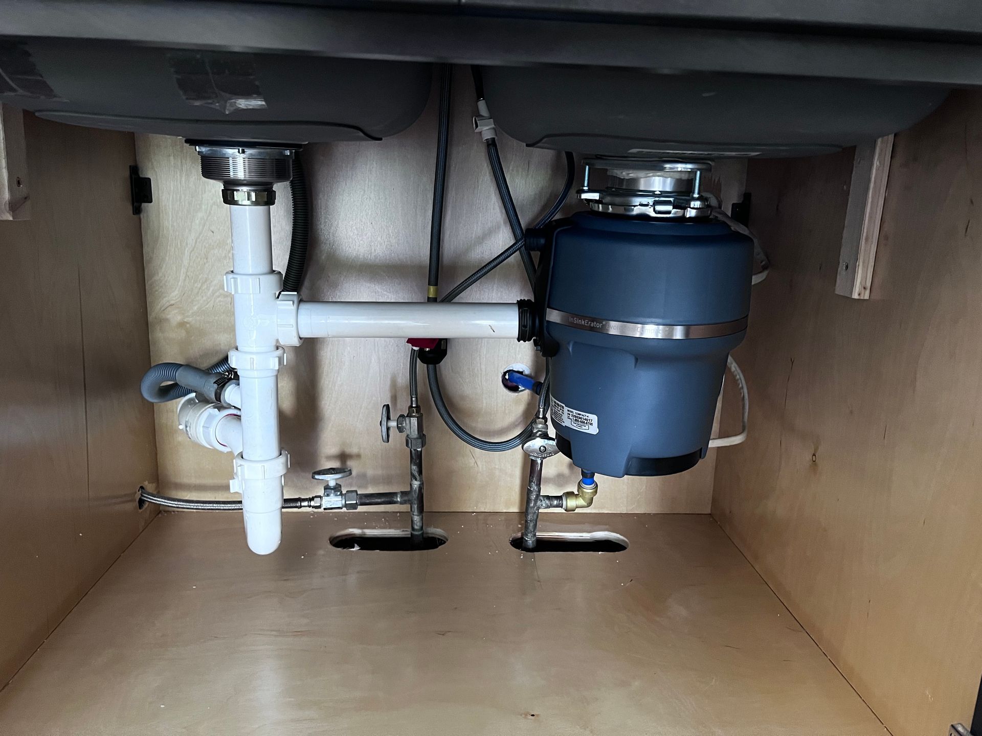 Under-sink plumbing with a garbage disposal and drain pipes, visible within a wooden cabinet.