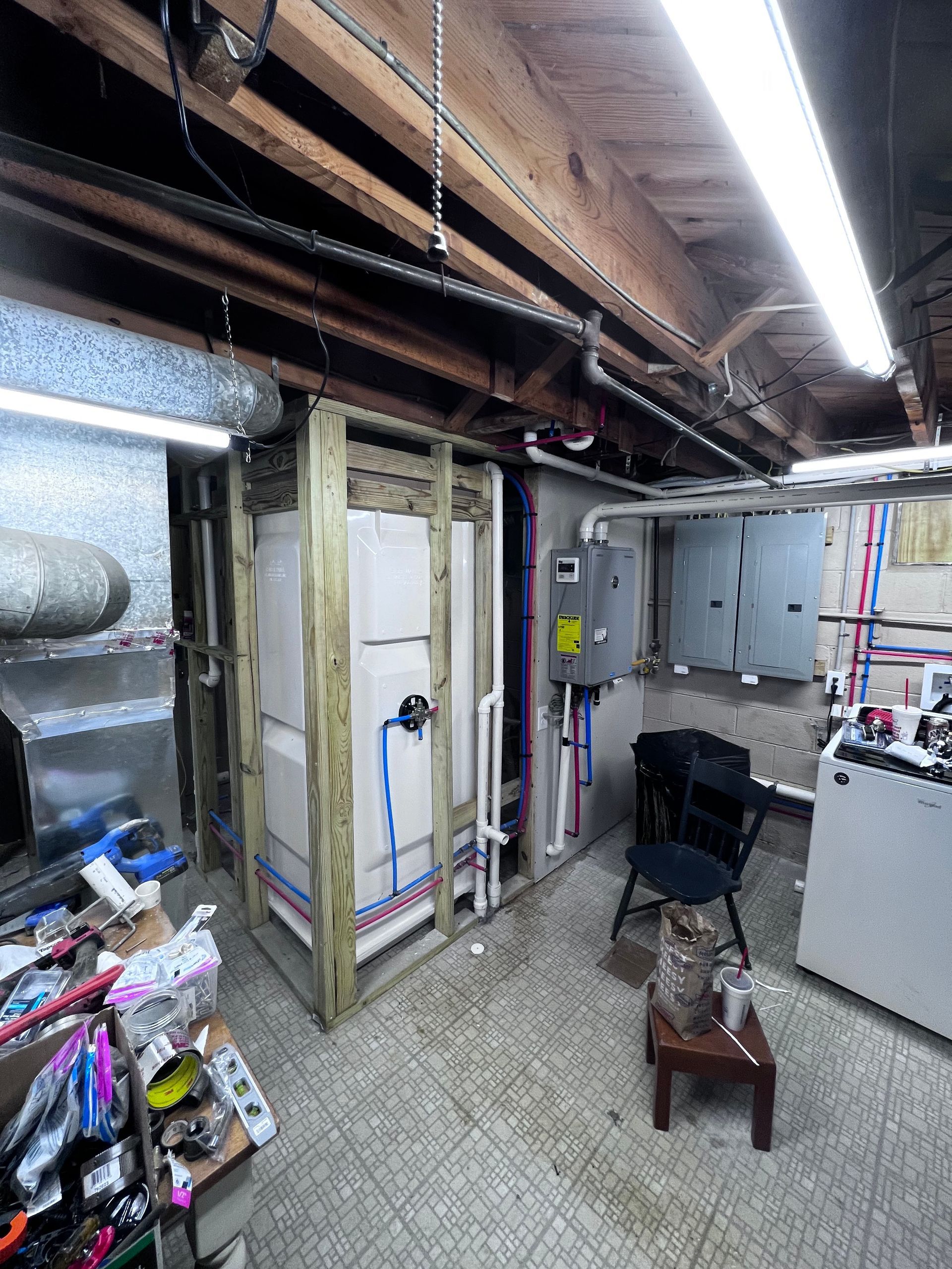 Basement with unfinished shower frame, exposed pipes, electrical panels, and cluttered work area.