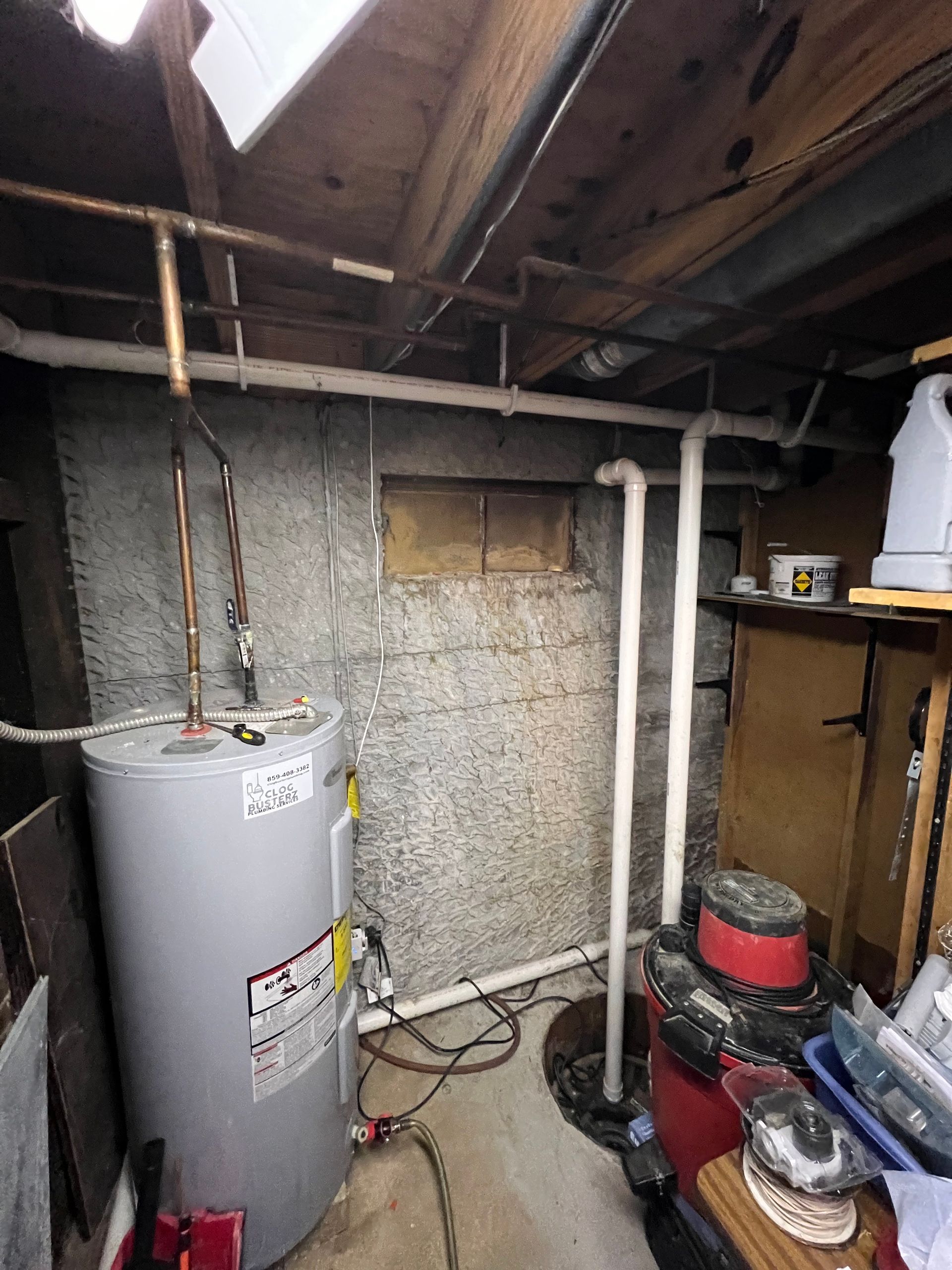 Basement with a water heater, pipes, and tools near a cinder block wall.