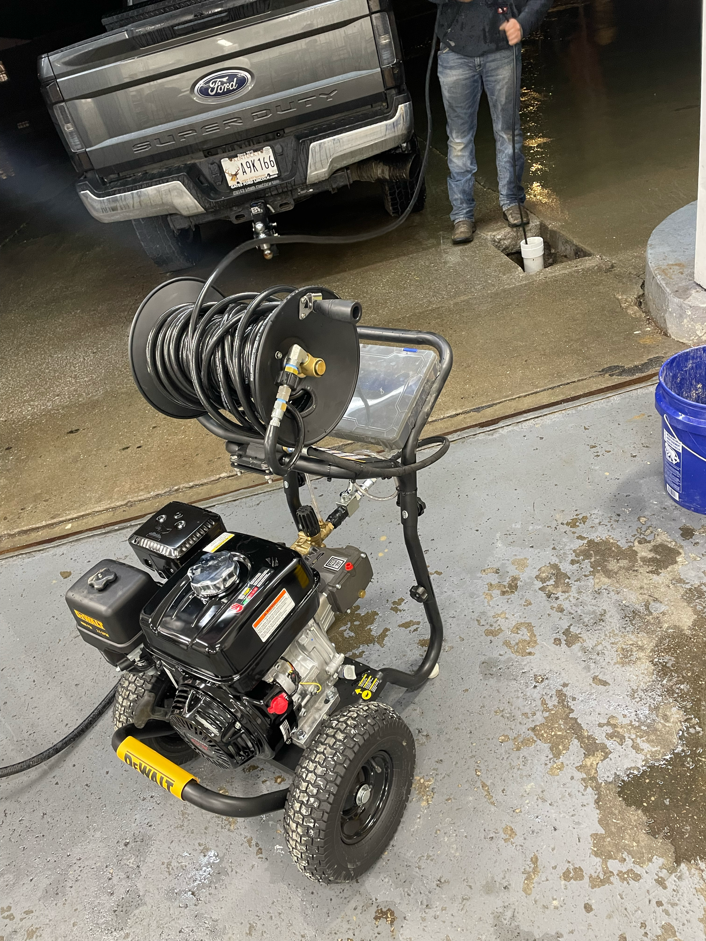 A gas-powered pressure washer washing a pickup truck in a car wash bay.