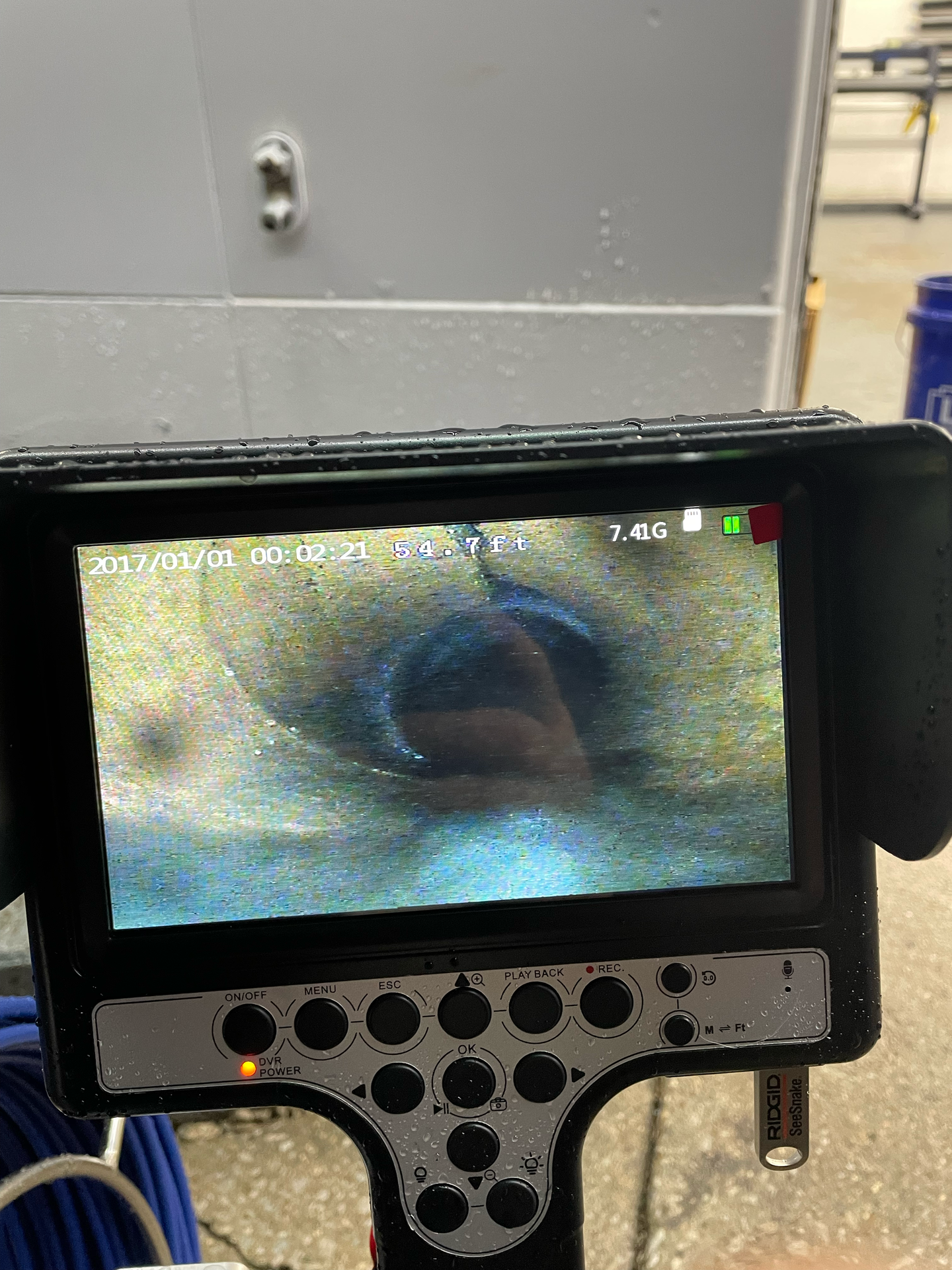 A monitor displays an endoscopic view inside a pipe.  The opening is circular, surrounded by brown and blue.