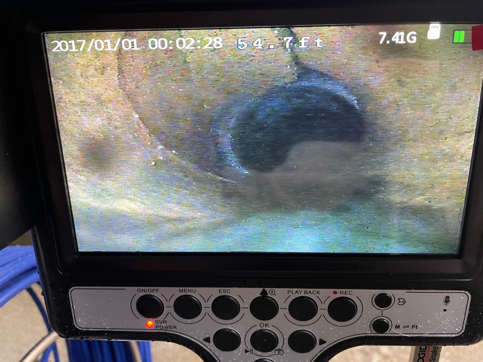 A screen displaying a pipe inspection camera view. The dark pipe is centered, and it has dated timestamp at the top.
