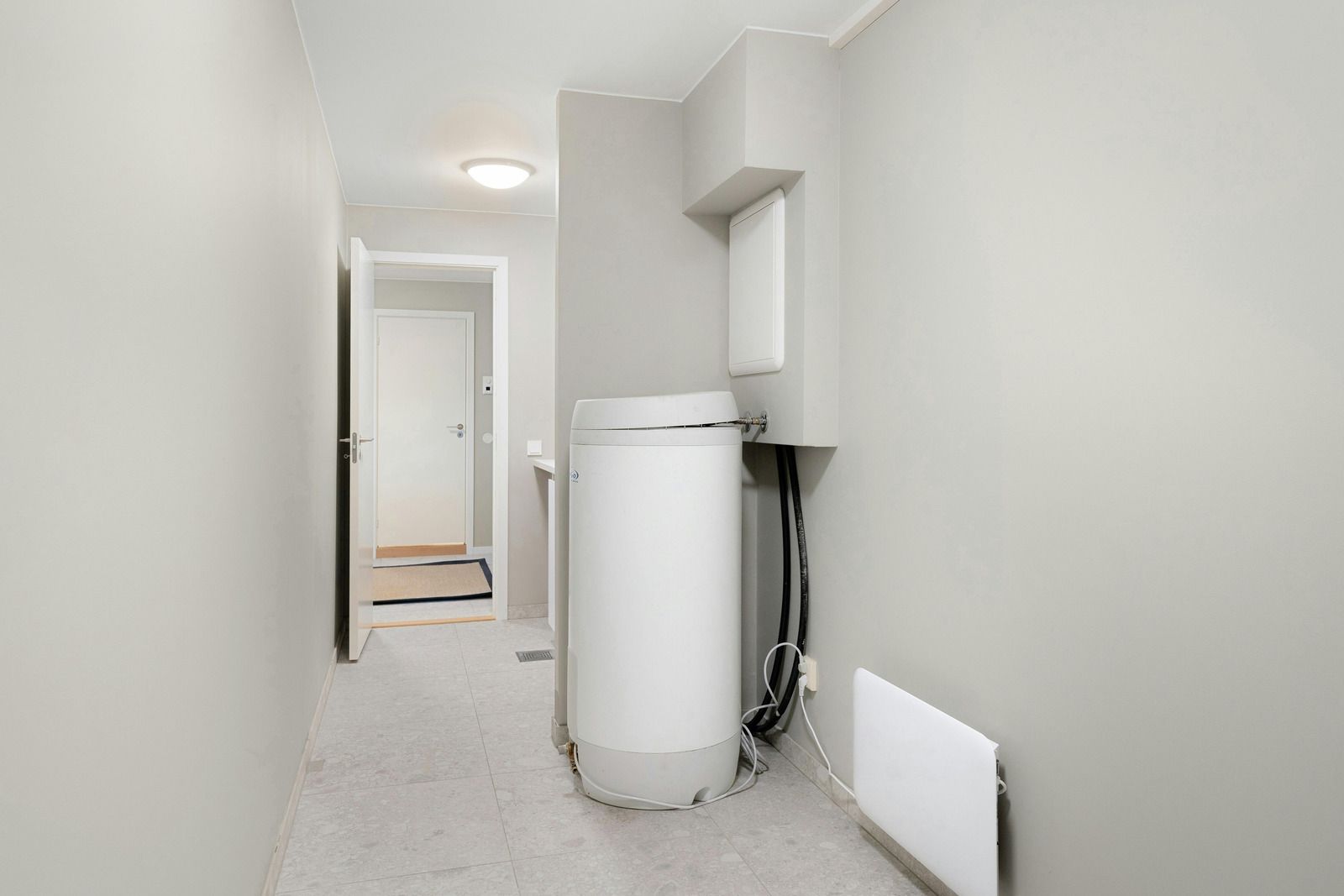Narrow hallway with a white water heater and an open door at the end. Gray walls and flooring.