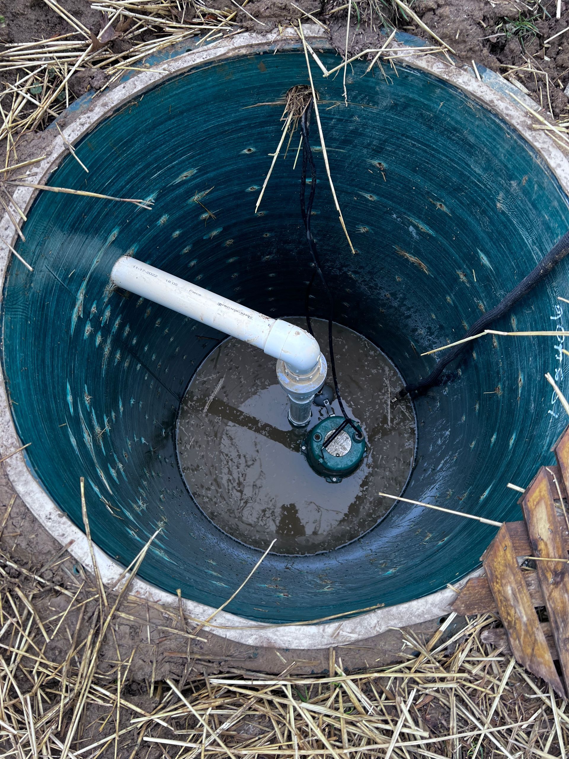 Looking down into a green septic tank with a white pipe and a submerged pump.