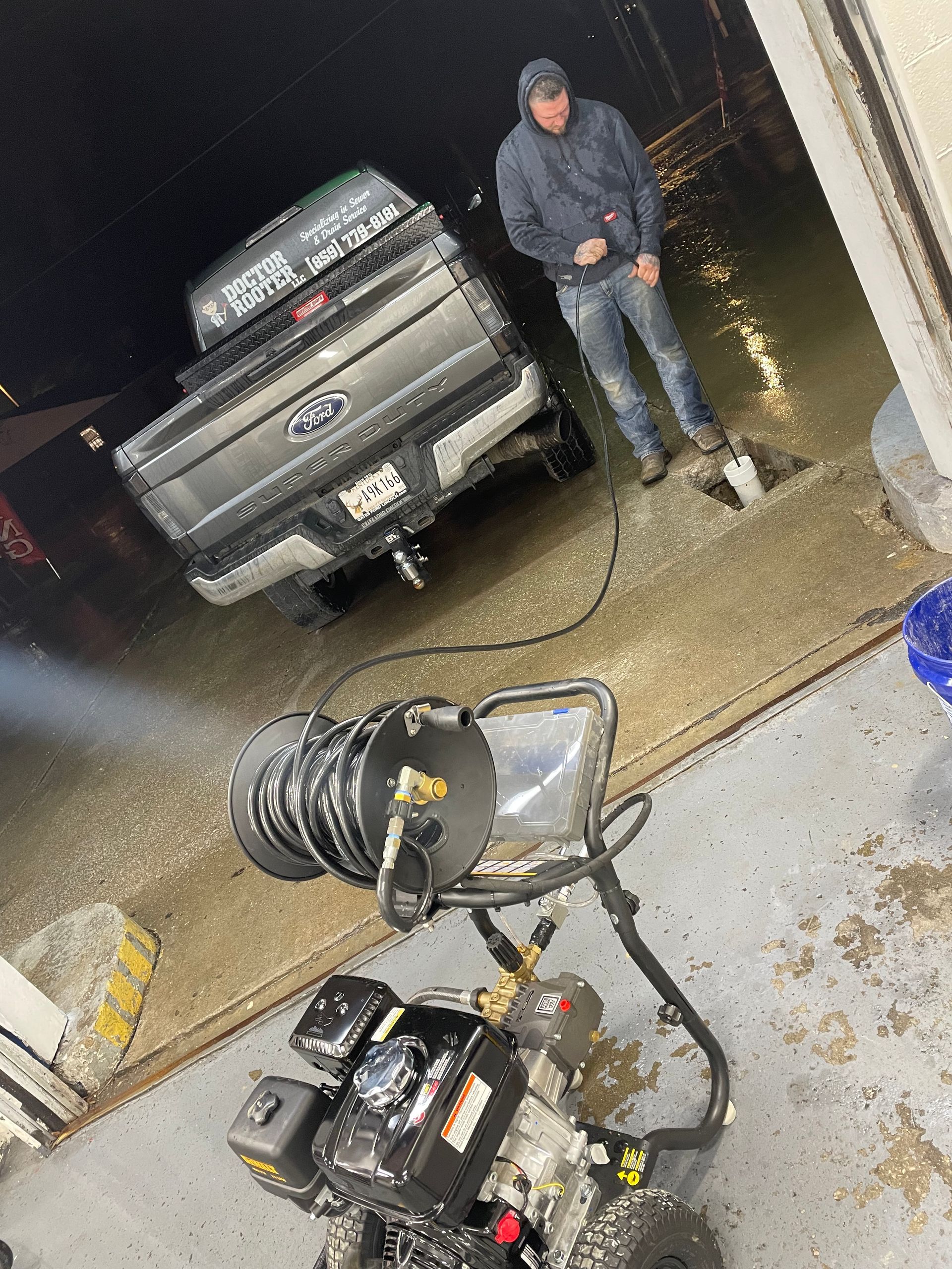 Man pressure washing a truck in a flooded, wet area. Black pressure washer machine in foreground. Dark, night setting.
