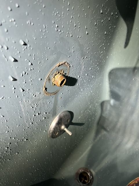 Close-up of a rusty pipe fitting and a metal peg attached to a gray surface, possibly a tub.