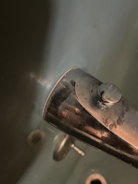 Close-up of a tarnished metal pipe with a circular cap, likely part of an appliance or fixture.