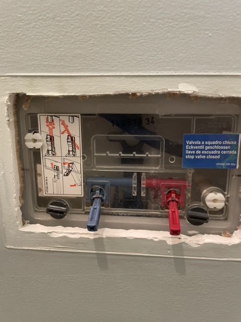 Recessed toilet flush mechanism with blue and red levers and instruction labels.