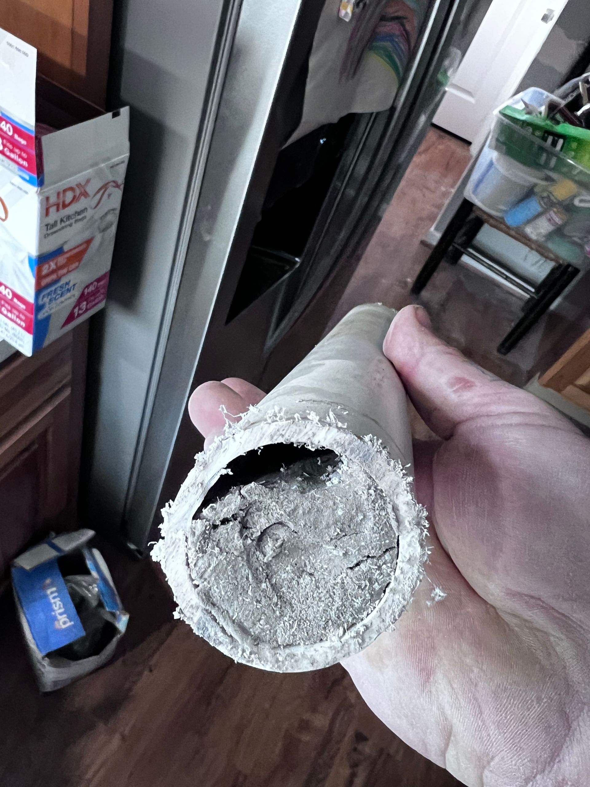Hand holding a cut section of a gray, cylindrical object; possibly a pipe. The inside is filled with a dense, gray material.