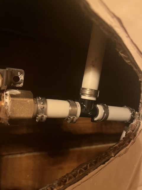 Pipes with metal clamps and a black T-connector inside a brown cardboard box.