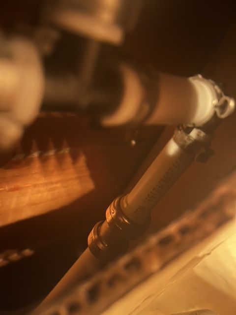 Close-up of a pipe with connectors, lit by warm light, inside a wooden structure.
