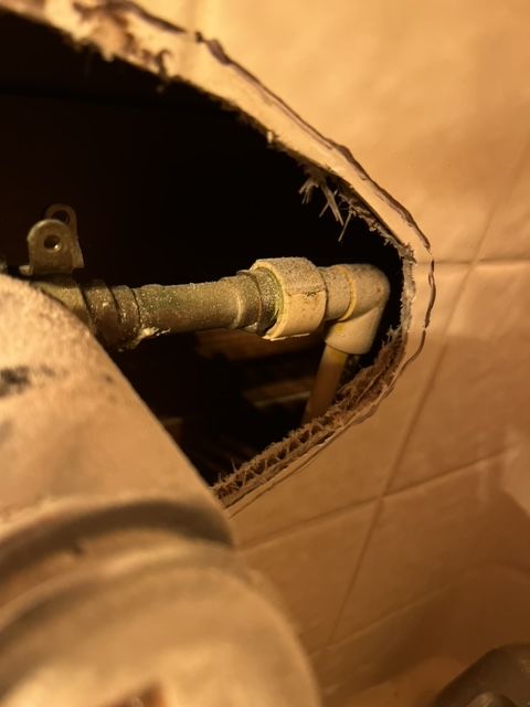 Plumbing pipes emerging from a wall, visible through a rough opening in the tile.