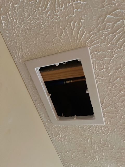 White rectangular vent frame in textured ceiling with open dark interior.