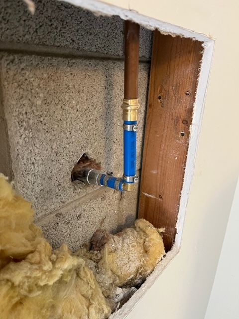 Copper pipe and blue PEX pipe with fittings in a wall cavity. Insulation and a wooden support are visible.