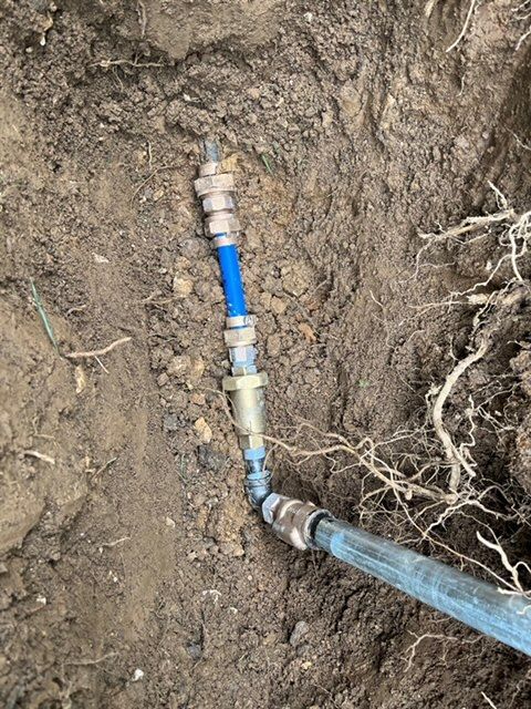 Underground pipe connections with metal and blue tubing, exposed in dirt.