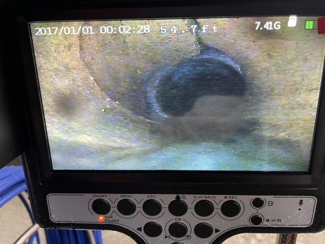 Camera view of a pipe interior, showing a dark hole in a light-colored surface; display with date and depth.