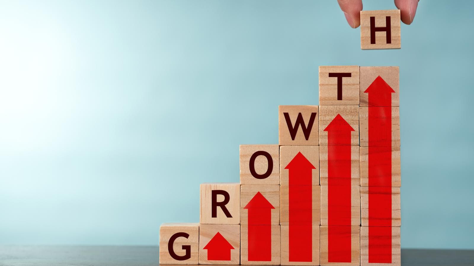 A person is holding a wooden block with the letter h on top of a wooden block with the word growth on it.