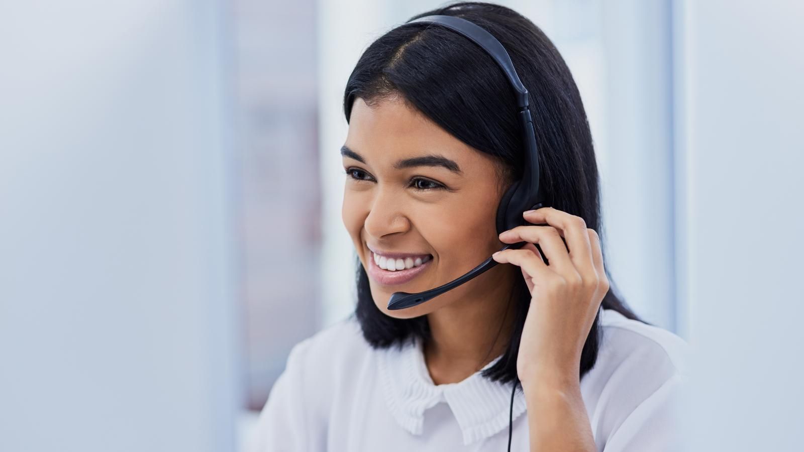 how to reduce labor costs Woman wearing a headset, smiling, looking at a computer screen.