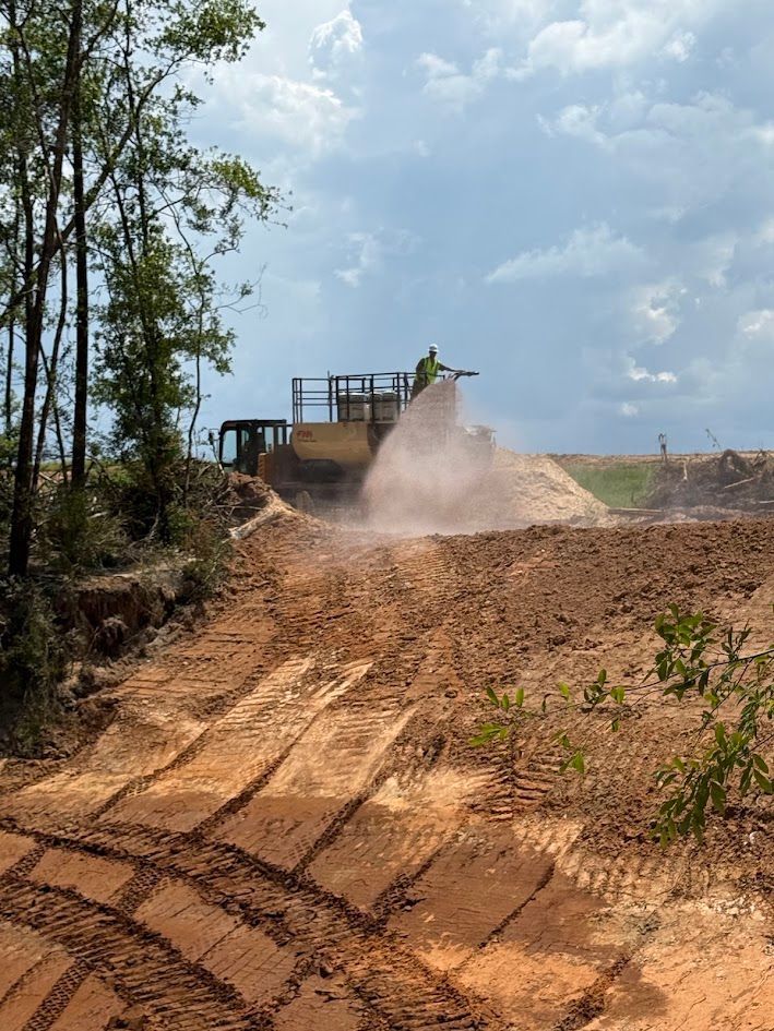 Deep dirt trench with tracked vehicle marks through a wooded area under construction