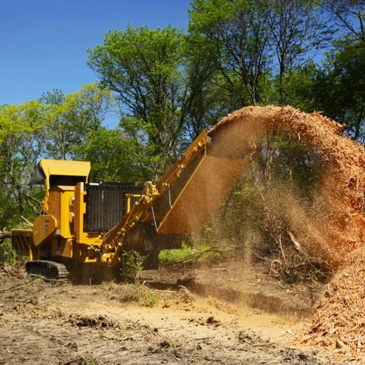 Wood processing machine feeding cut logs into a pile, with workers in safety vests at a lumberyard