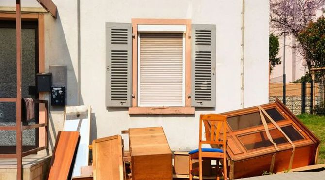 Piles of broken wooden furniture and shutters leaning against a house wall outside.