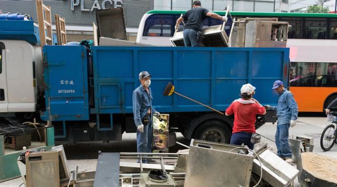 Workers loading debris into a blue dump truck on a city street