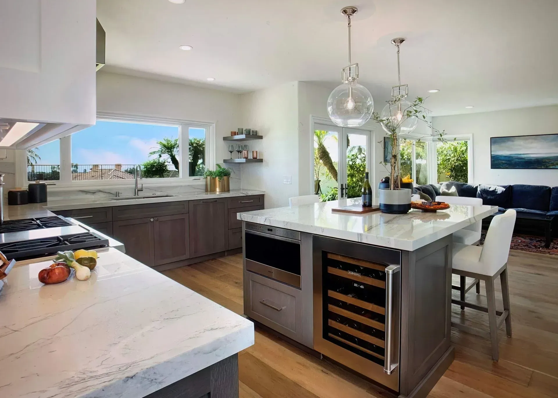 Modern kitchen with island, marble countertops, wine cooler, and views.