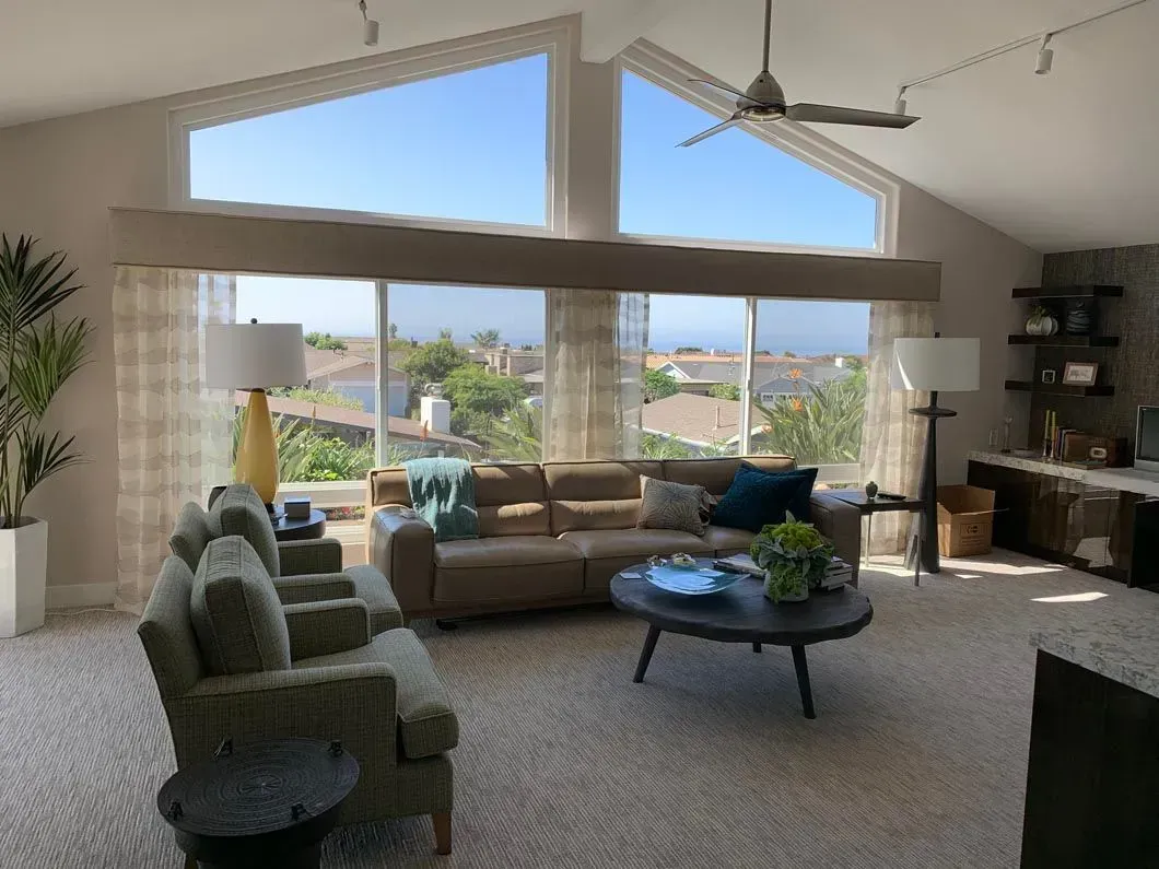 Living room with tan sofa, armchairs, large windows with ocean view, and neutral decor.