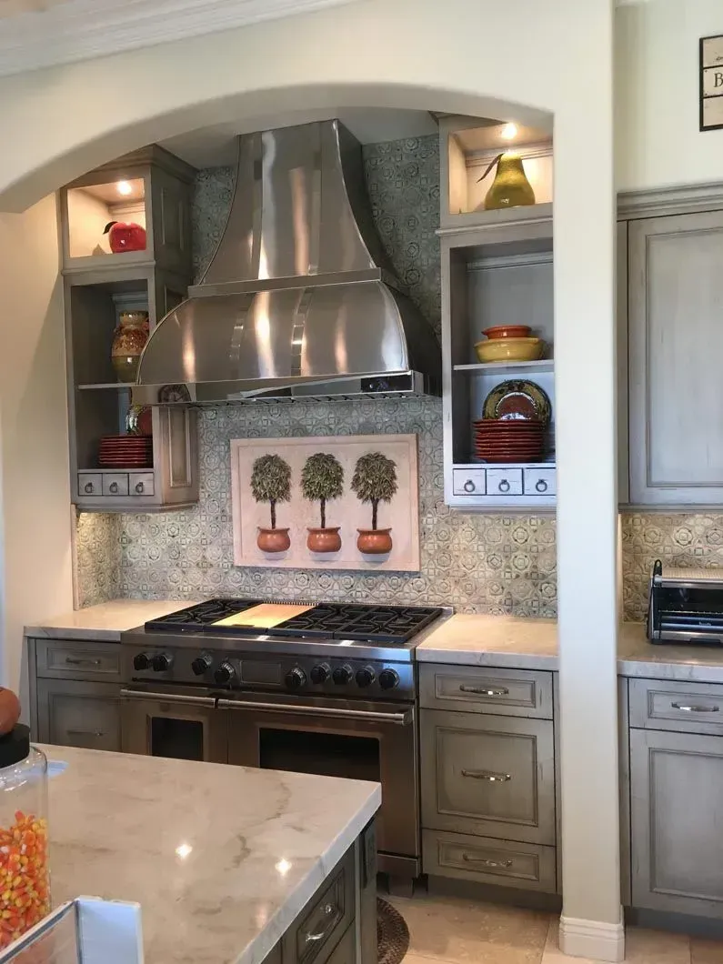 Stainless steel range hood over stove in a kitchen with gray cabinets and marble countertops.
