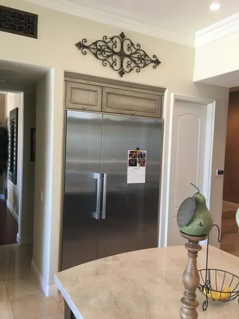 Stainless steel refrigerator with decorative embellishment above in kitchen.